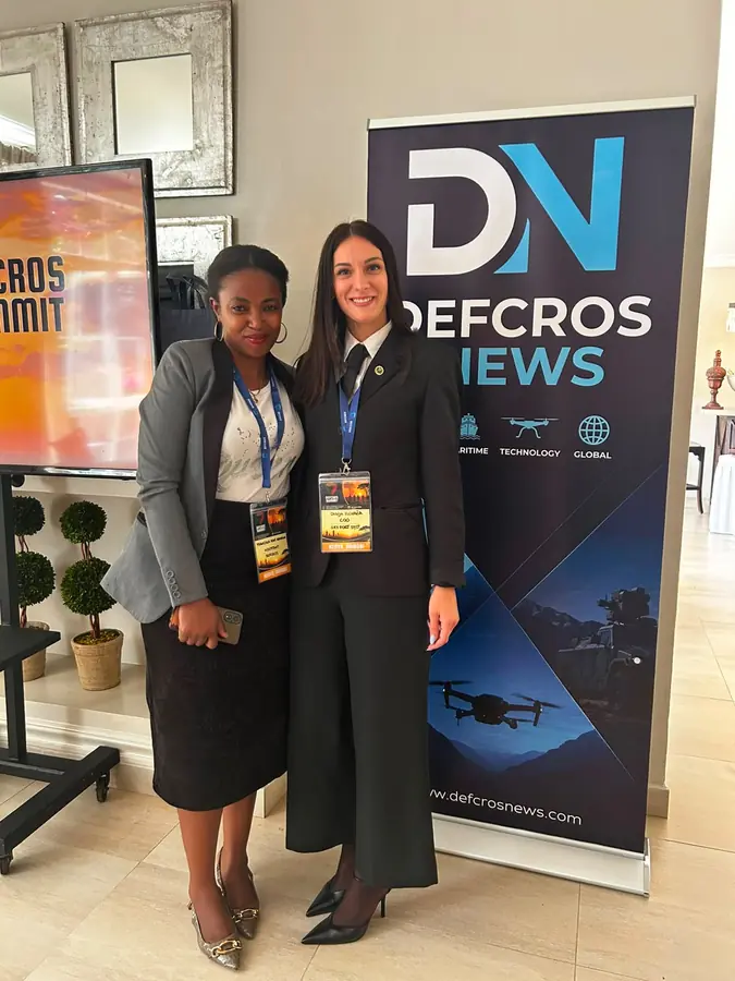 Two delegates in front of the DEFCROS News banner